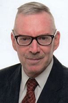 Porträt eines älteren Mannes mit Brille, Schnurrbart und Anzug mit rot gemusterter Krawatte.