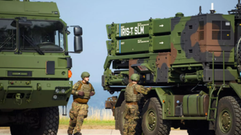 Soldaten stehen neben zwei Militärlastwagen, einer mit IRIS-T SLM Raketenwerfern.