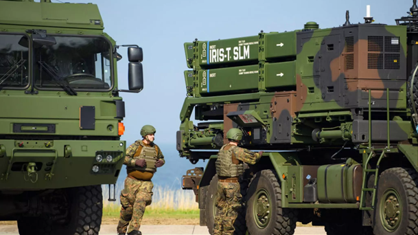 Soldaten stehen neben zwei Militärlastwagen, einer mit IRIS-T SLM Raketenwerfern.