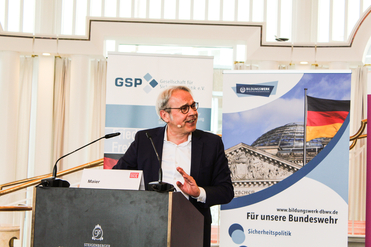 Mann Maier spricht an Rednerpult, dahinter Banner der Gesellschaft für Sicherheitspolitik und Bundeswehr Bildungswerk.