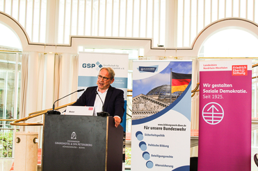 Mann, Maier, spricht am Rednerpult bei Steigenberger, umgeben von GSP, Bundeswehr und Friedrich Ebert Stiftung Bannern.