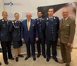 Gruppe: vier junge Leute in Bundeswehr-Uniformen und zwei Männer in Anzügen, vor einem Banner der Gesellschaft für Sicherheitspolitik.