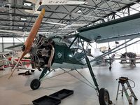 Ein grünes und blaues Oldtimer-Propellerflugzeug mit freiliegendem Sternmotor und Holzpropeller im Museumshangar.
