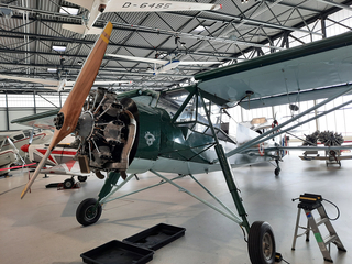 Ein grünes und blaues Oldtimer-Propellerflugzeug mit freiliegendem Sternmotor und Holzpropeller im Museumshangar.