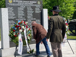 Ein Soldat und ein Zivilist ehren Gefallene an einem Denkmal mit Namen und einem Blumenkranz zum Gedenktag.