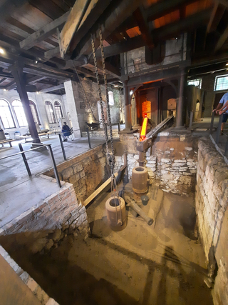 Historische Schmiede oder Gießerei mit glühendem Ofen, Ketten und alten Geräten in einer Grube.