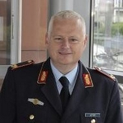 Porträt eines lächelnden Mannes mit grauem Haar in dunkler deutscher Militäruniform mit goldenen und roten Abzeichen.