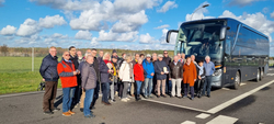 Fröhliche Reisegruppe älterer Menschen posiert vor einem dunklen Reisebus an einem sonnigen Tag.