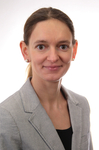 Professionelles Porträt einer lächelnden Frau mit braunen Haaren, gestreiftem Blazer und Perlohrringen.
