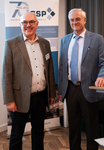 Josef Schmieder und ein weiterer Mann lächeln auf einer GSP-Veranstaltung zur Sicherheitspolitik vor einem 70-Jahre-Banner.