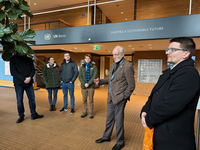 Eine Gruppe Menschen hört einem Mann in der UN Bonn Lobby zu, mit einem Schild 'Shaping a Sustainable Future' darüber.