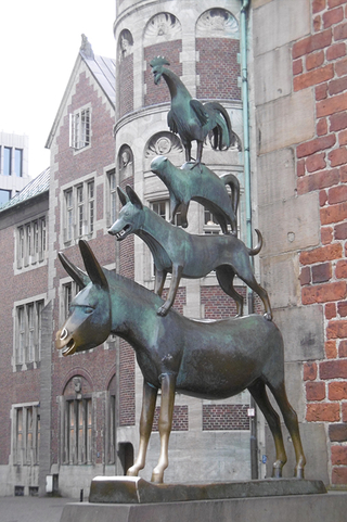 Bronzestatue der Bremer Stadtmusikanten: Esel, Hund, Katze und Hahn übereinander gestapelt, vor Backsteingebäuden.