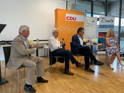 Vier Personen bei einer Podiumsdiskussion mit CDU- und GSP-Bannern im Hintergrund.