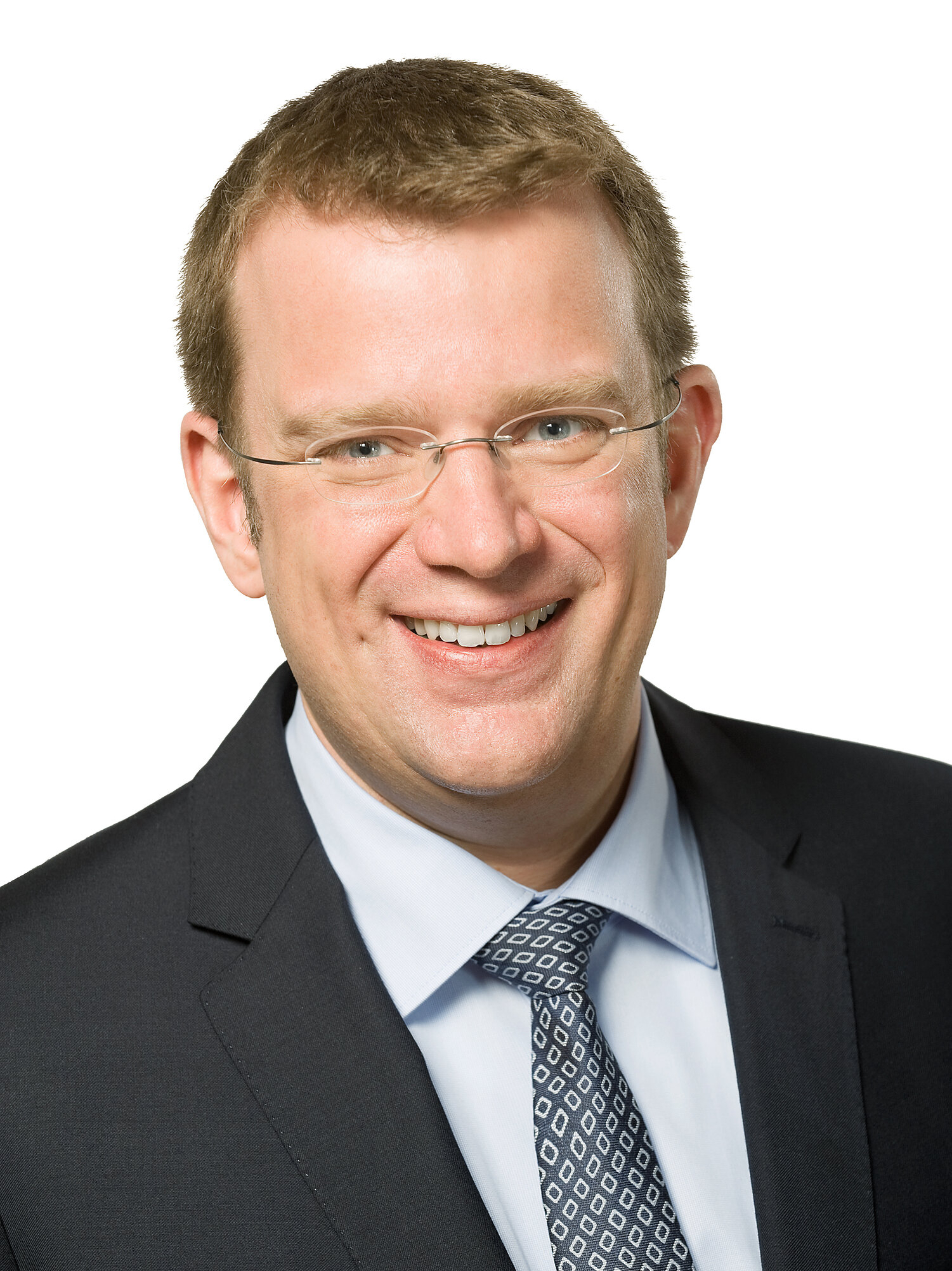 Porträt eines lächelnden kaukasischen Mannes mit kurzen braunen Haaren und randloser Brille, im dunklen Anzug mit Hemd und Krawatte.