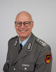 Lächelnder kahlköpfiger Mann mit Brille in grauer deutscher Militäruniform, mit Abzeichen auf Revers und Schultern.