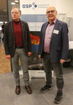 Zwei Männer, darunter Josef Schmidhofer, stehen vor einem GSP (Gesellschaft für Sicherheitspolitik) Banner bei einer Veranstaltung.