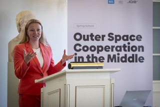 Eine Frau im korallfarbenen Blazer spricht an einem Rednerpult vor einem Banner mit "Outer Space Cooperation".