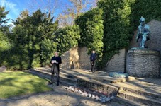 Zwei Männer an einem Kriegsdenkmal mit kniender Soldatenstatue und Gedenkmohnblumen.