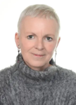 Porträt einer Frau mit sehr kurzen silbernen Haaren, grünen Augen und einem grauen Struktorpullover, blickt nach vorne.