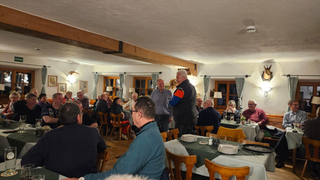 Eine Gruppe von Menschen versammelt sich in einem rustikalen Restaurant, einige sitzen an Tischen, andere unterhalten sich stehend.