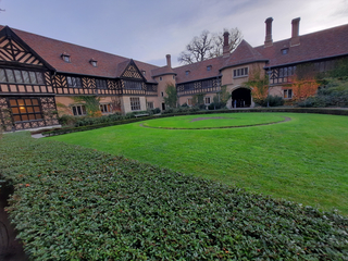 Innenhof der Wannsee Villa in Berlin, ein historisches Fachwerkgebäude mit grünem Rasen und Hecken unter bewölktem Himmel.