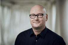 Lächelnder glatzköpfiger Mann mit schwarzer Brille und schwarzem Hemd.