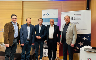 Fünf lächelnde Männer posieren vor Bannern der Gesellschaft für Sicherheitspolitik und des Deutsch-Amerikanischen Instituts.