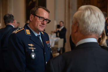 Ein lächelnder Mann in dunkler Bundeswehr-Uniform mit Brille spricht mit einer Person, deren Hinterkopf sichtbar ist.