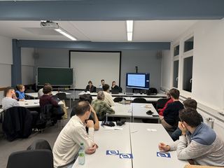 Eine Gruppe von Personen sitzt in einem Klassenzimmer und nimmt an einer Präsentation über die "Talk to the City"-Plattform teil.