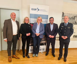 Fünf Personen, darunter ein Polizist, posieren vor einem GSP-Banner für Sicherheitspolitik.