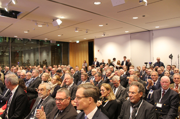 Zahlreiche Fachleute sitzen in Reihen in einem modernen Konferenzsaal, viele tragen Ausweise, bei einer Veranstaltung.