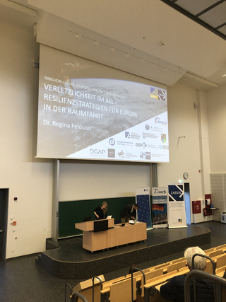 Ein Hörsaal mit einer Präsentation über „Europas Zukunft im Weltraum: Resilienzstrategien“ auf einer großen Leinwand.