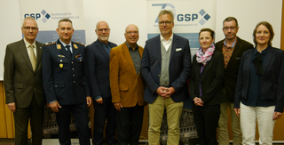 Eine Gruppe von neun Personen, darunter ein Mann in Uniform, steht lächelnd vor einem GSP-Veranstaltungsbanner.