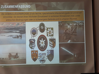 Präsentationsfolie über Gebirgsjägerbrigade 23 mit Textzusammenfassung, Bildern von Einsätzen und Abzeichen.