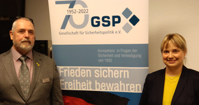 Ein Mann und eine Frau vor einem GSP-Banner zum 70-jährigen Jubiläum der Gesellschaft für Sicherheitspolitik.