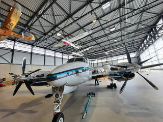 Innenansicht eines Luftfahrtmuseums mit einem großen weißen Propellerflugzeug und vielen kleineren Flugzeugen unter dem Hallendach.