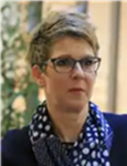 Kopfaufnahme einer Frau mit kurzen Haaren und Brille, die einen blau gepunkteten Schal und ein dunkles Oberteil trägt.