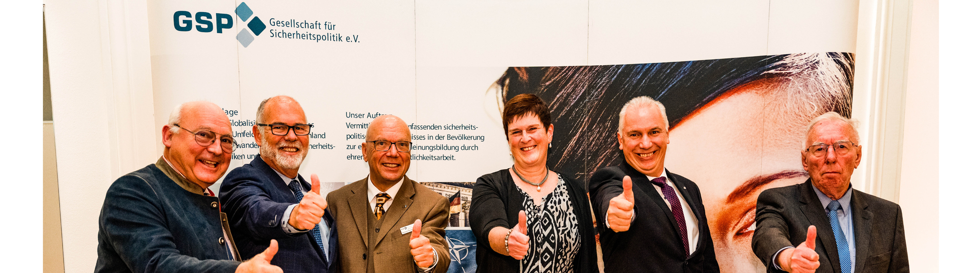 Sechs Personen zeigen Daumen hoch vor dem GSP-Ausstellungsbanner der Gesellschaft für Sicherheitspolitik e.V.