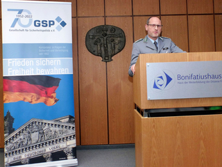 Deutscher Militäroffizier spricht am Rednerpult im Bonifatiushaus. Ein GSP-Banner mit Reichstagsgebäude ist sichtbar.
