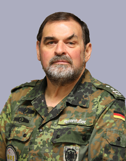 Porträt eines Mannes in deutscher Bundeswehr-Flecktarnuniform mit Bart, Namensschild "Rottenfußßer" und Deutschlandflagge.