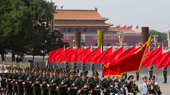 Chinesische Militärparade: Uniformierte Soldaten marschieren mit Gewehren und roten Flaggen vor dem Tiananmen-Tor mit Mao-Porträt.