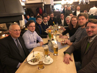 Eine Gruppe von Menschen sitzt an einem Tisch in einer traditionellen Gaststätte, isst und trinkt Bier.