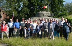 Eine Gruppe Senioren steht auf einer Wiese vor einem Militärpanzer mit belgischer und amerikanischer Flagge.