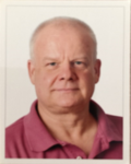 Kopfaufnahme eines Mannes mittleren Alters mit kurzen weißen Haaren und blauen Augen, der ein rosa Poloshirt trägt und in die Kamera blickt.