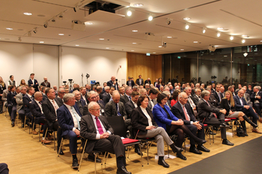 Ein großes Publikum von Erwachsenen in Business-Kleidung, das an einer Konferenz teilnimmt und nach vorne blickt.