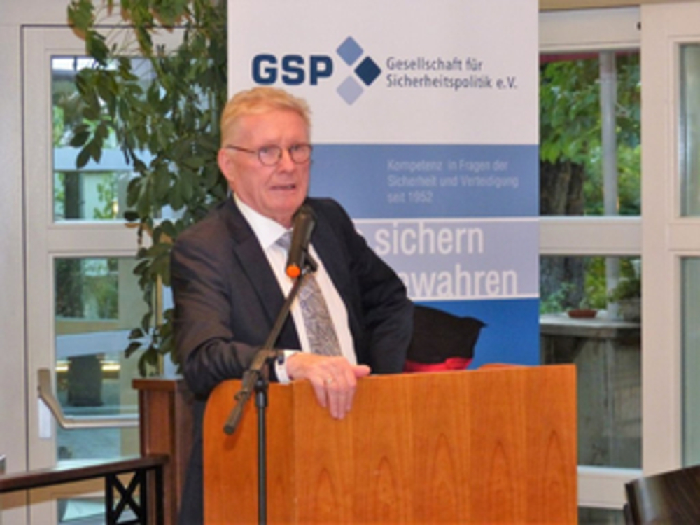 Ein älterer Mann im Anzug spricht an einem Holzrednerpult vor einem Banner der 'GSP Gesellschaft für Sicherheitspolitik'.