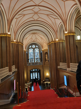 Elegante Halle mit rotem Teppich, gewölbten Decken, verzierten Säulen, Buntglasfenstern und einer klassischen Statue.