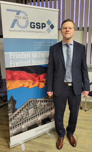 Mann im Anzug vor GSP-Banner zum 70-jährigen Jubiläum mit deutscher Flagge und Reichstagsgebäude.