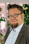 Porträt eines lächelnden Mannes mit Brille, Ziegenbart und kariertem Hemd.