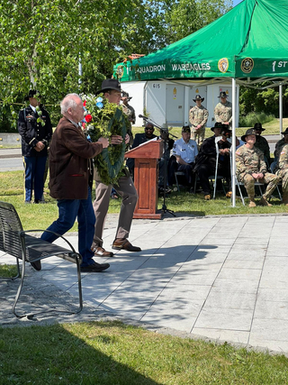 Bei einer Militärzeremonie im Freien tragen ein älterer Mann und ein Kavalleriesoldat mit Stetson einen großen Kranz.